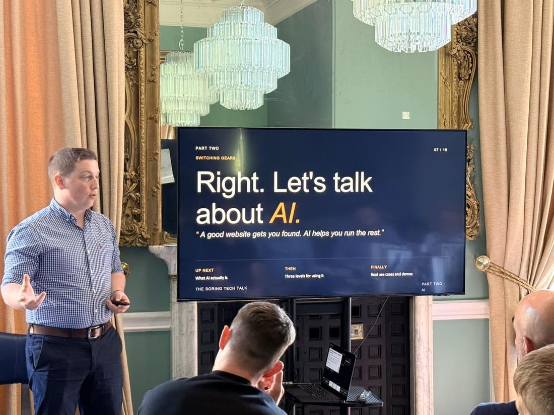 Sam Jenkins presenting on practical AI for business, his slides on the screen behind him.